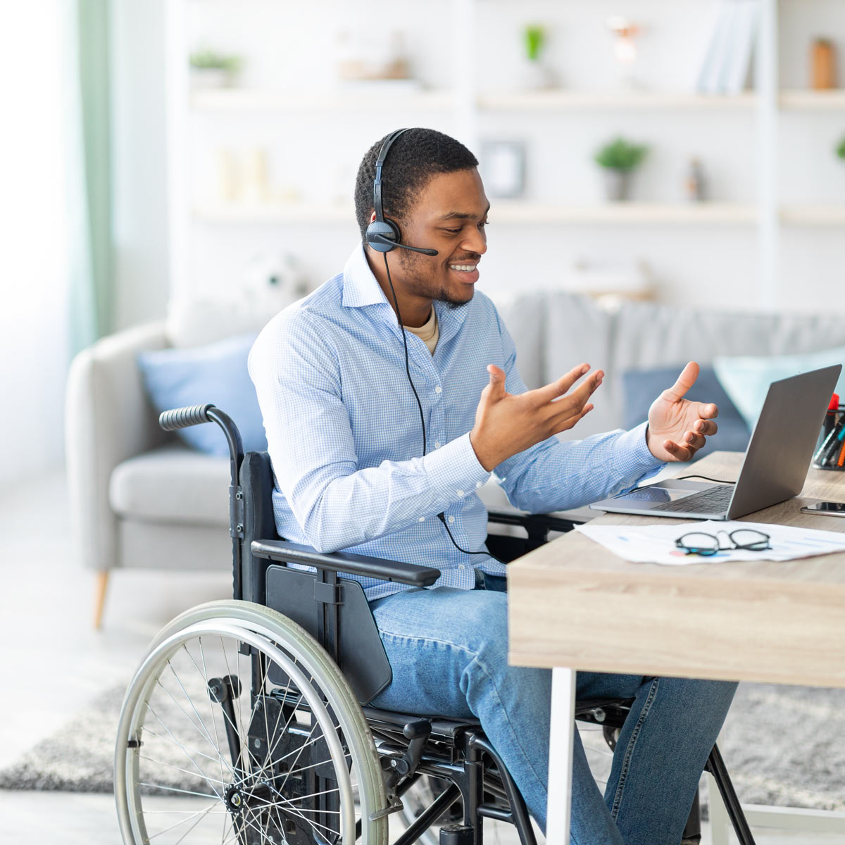 Man sitting in a wheelchair while speaking into a headset and gesturing to a computer screen