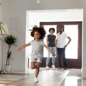 A young girl running down the hallway of her home as her parents watch from the doorway with smiles on their face