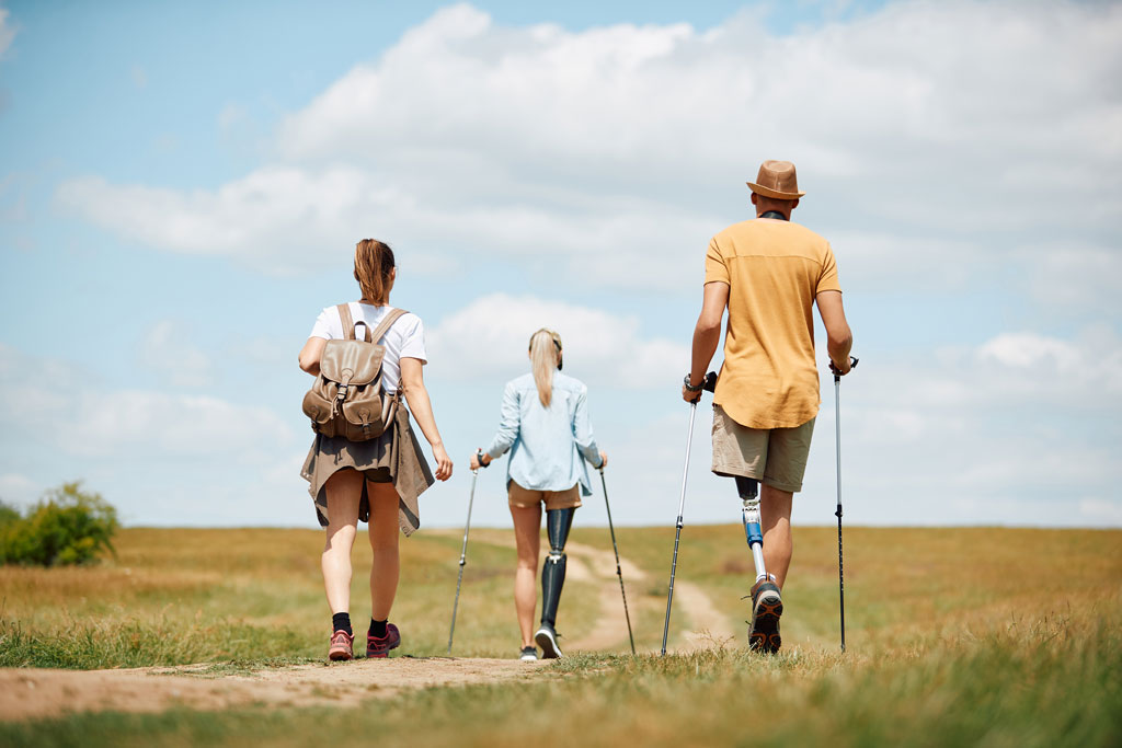 Hikers with prosthetic legs and walking sticks walking together through an open field